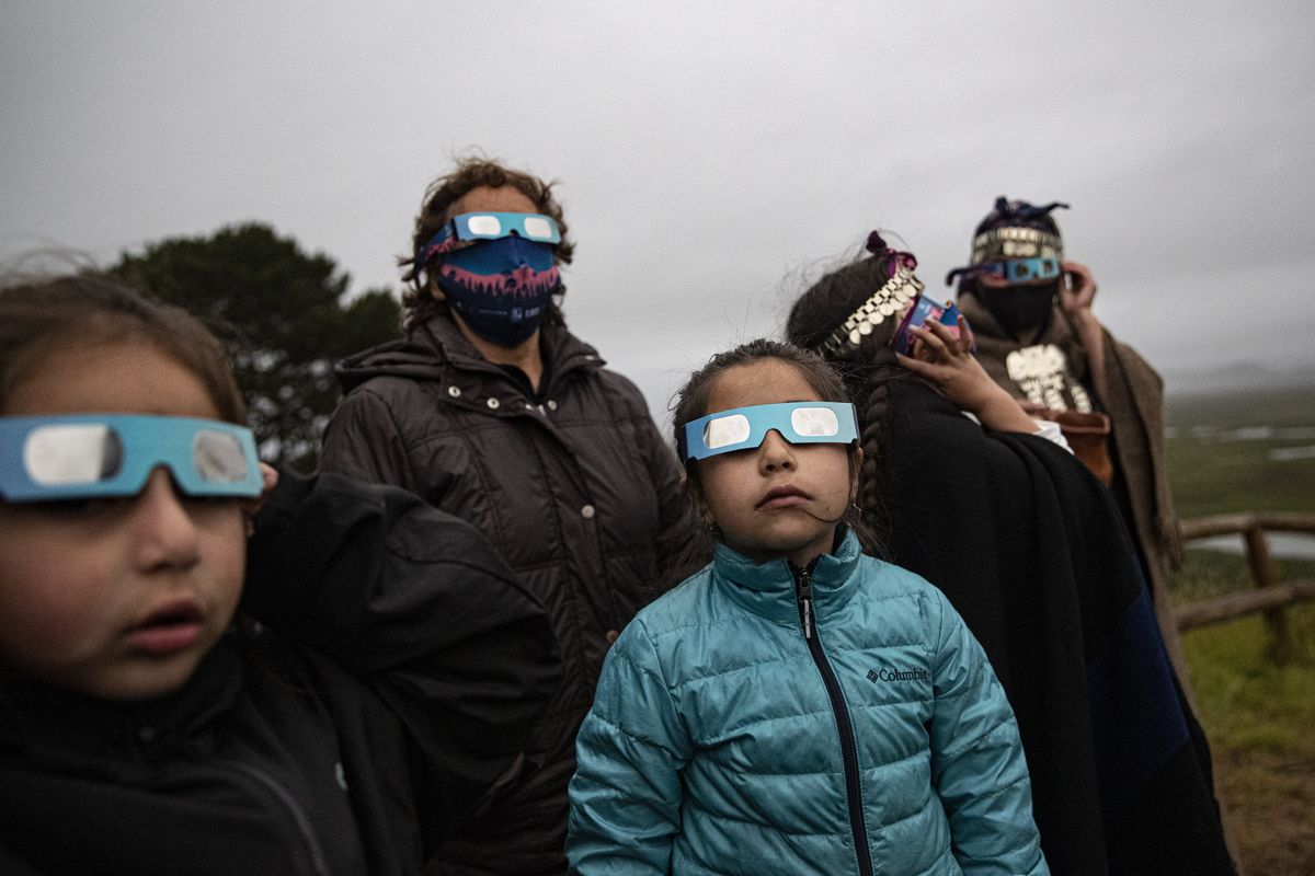 A Mapuche Indigenous family uses special glasses to try and observe a total solar eclipse in Carahue, La Araucania, Chile, Monday, Dec. 14, 2020. The total eclipse was not visible from Carahue because of an overcast sky.  (Esteban Felix)