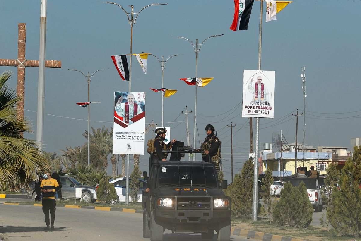 Iraqi security forces pass by Iraq and the Vatican flags and posters announcing visit of the Pope Francis in a street in Qaraqosh, Iraq, Monday, Feb. 22, 2021.  (Hadi Mizban)