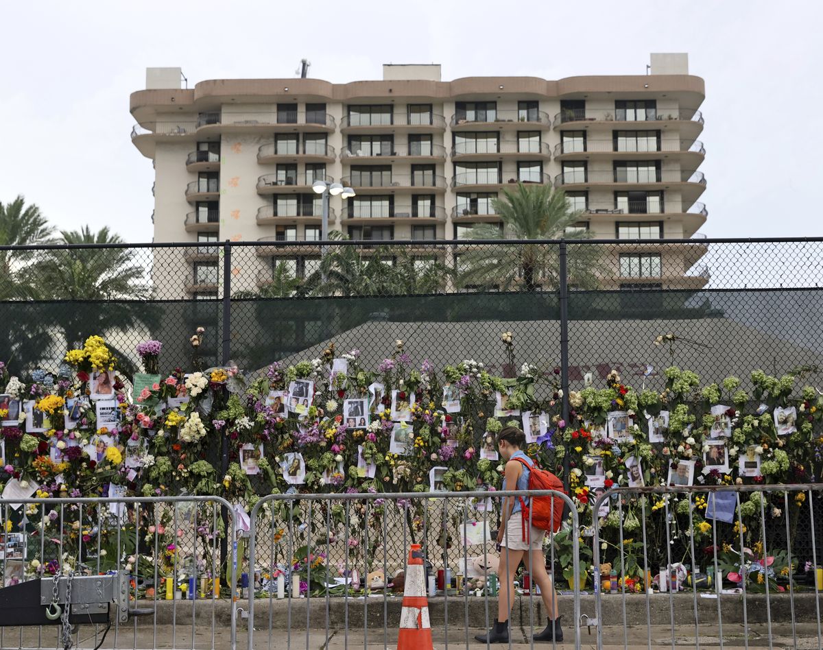 FILE - In this Wednesday, June 30, 2021, file photo, an unidentified woman visits the memorial wall full of photos of the missing and messages of love, support and prayers at Harding Avenue and 86th Street as search and rescue personnel continue to look for survivors in the rubble of the Champlain Towers South Condo in Surfside, Fla. Even as the search continues over a week later for signs of life in the mangled debris, the process of seeking answers about why it happened and who is to blame is already underway in Florida's legal system.  (David Santiago)