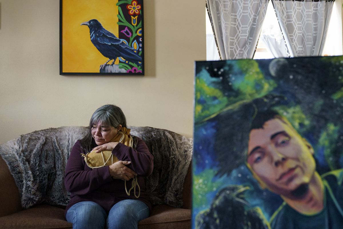 Rachel Taylor clutches a buckskin satchel filled with the ashes of her son, Kyle "Little Crow" Domrese, pictured at right, who died of an overdose, as she sits in the home they shared in Bemidji, Minn., Wednesday, Nov. 17, 2021. Just weeks remained until the anniversary of the day she opened his bedroom door and found her son face-down on his bed, one of more than 100,000 Americans lost in a year to overdoses as the COVID-19 pandemic aggravated America