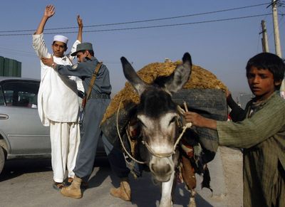 An Afghan boy walks with his donkey as a police officer frisks another on Saturday at a checkpoint in Kabul, Afghanistan.  (Associated Press / The Spokesman-Review)