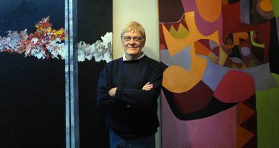 Roger Riggs, a retired art teacher, stands between two of his largest paintings  Dec. 23 at his home in south Spokane. He is a prolific painter in many different styles. The painting on the left he calls “9/11.” At right is “Africa Remembered.” (Jesse Tinsley / The Spokesman-Review)