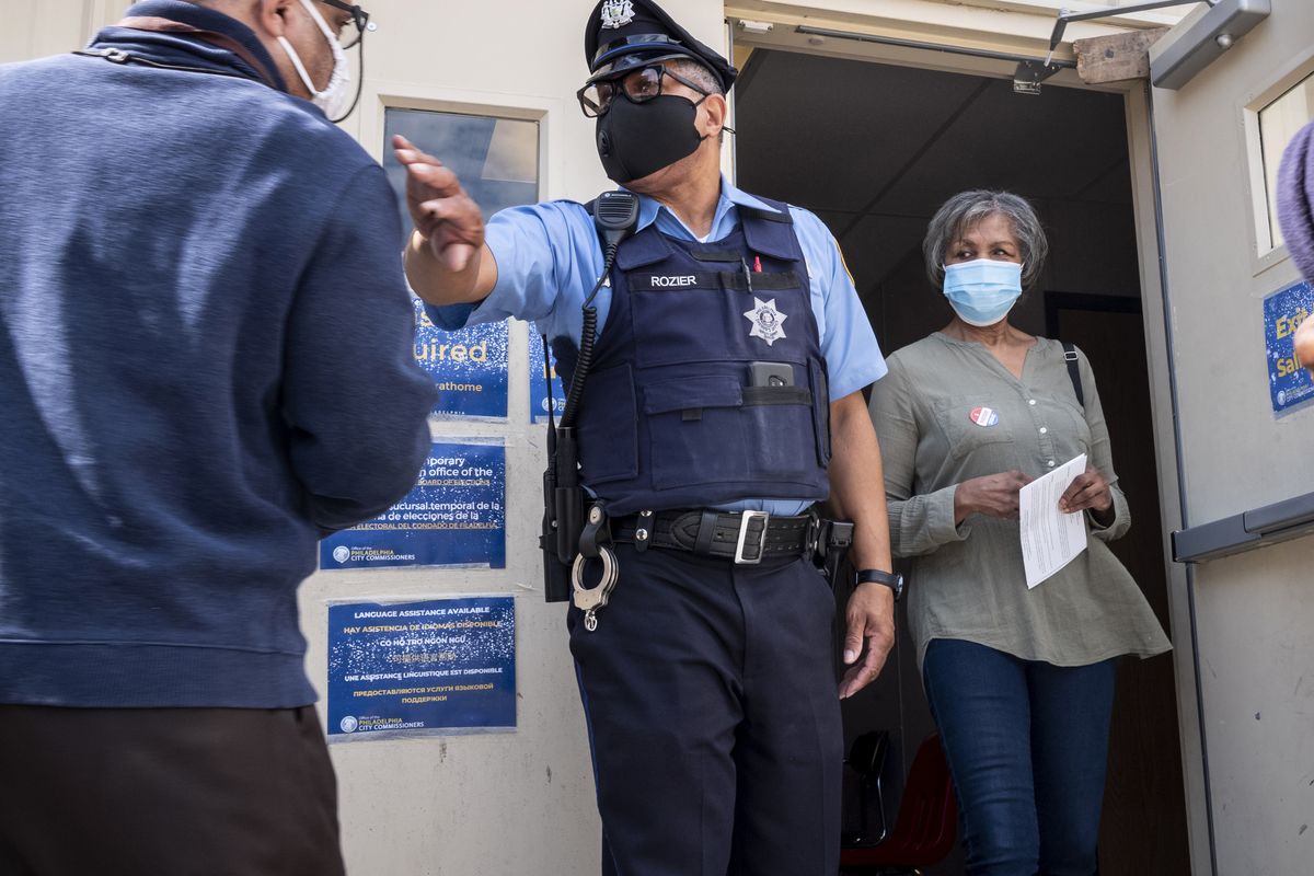 A Philadelphia Sheriff’s Deputy clears the door for a voter to exit at a satellite election office at Overbrook High School on Thursday in Philadelphia. The city of Philadelphia has opened several satellite election offices and more are slated to open in the coming weeks where voters can drop off their mail in ballots before Election Day. (Laurence Kesterson)
