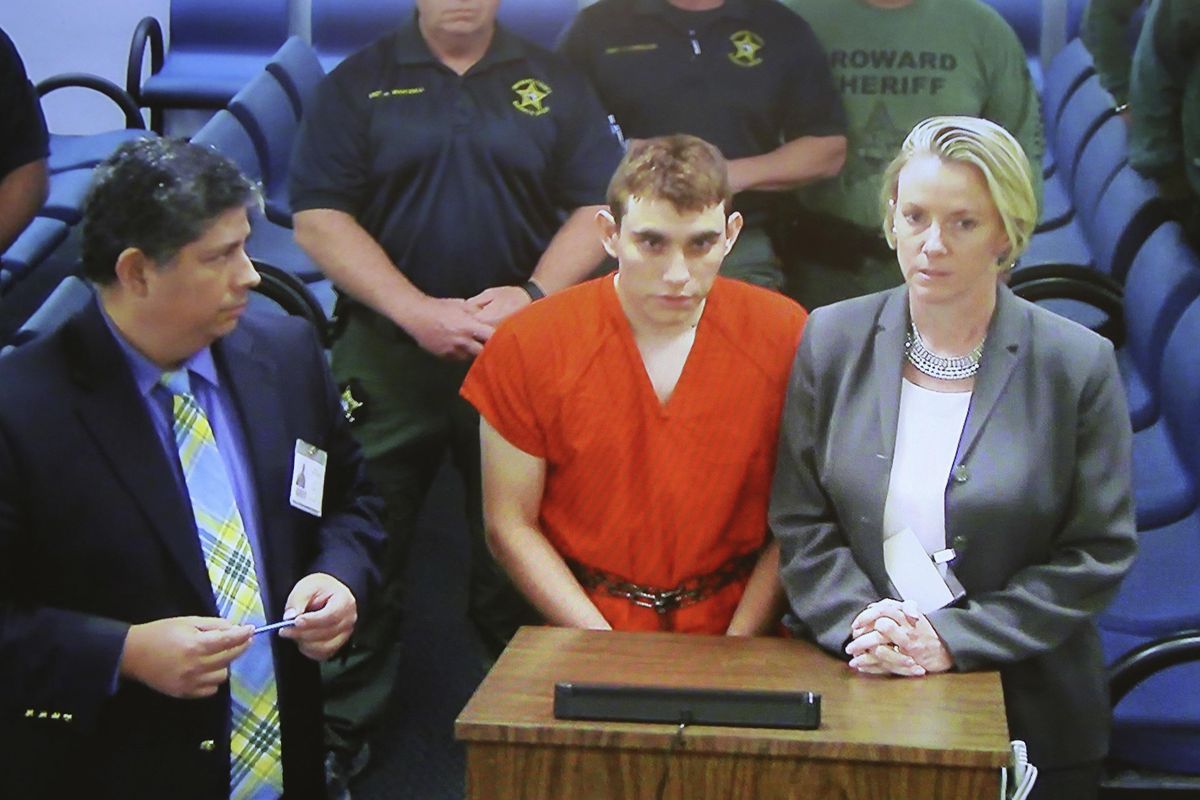 A video monitor shows school shooting suspect Nikolas Cruz, center, making an appearanceThursday, Feb. 15, 2018, before Judge Kim Theresa Mollica in Broward County Court, Thursday,  in Fort Lauderdale, Fla. Cruz is accused of opening fire Wednesday at Marjory Stoneman Douglas High School in Parkland, Fla., killing more than a dozen people and injuring several. (Susan Stocker / AP)
