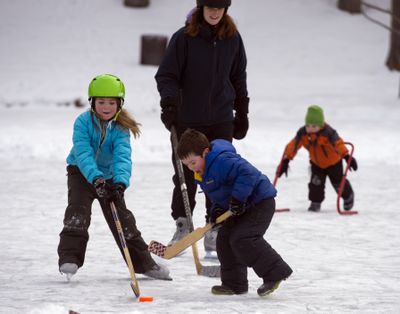 Olympians in training: Kayna Doolittle, left, 8, and her brother Kelton, 5, battle for the puck on the ice at Manito Park’s pond under the watchful eye of mother Heidi Doolittle on Sunday in Spokane. At right, friend Peter Dix, 5, plays on the ice. (Jesse Tinsley)