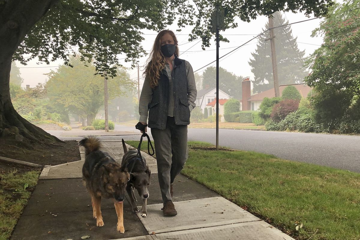 Zoe Flanagan walks her dogs amid dense smoke from wildfires in Portland, Ore., on Monday, Sept. 14, 2020. Wildfires across the U.S. West have created hazardous air quality in Portland and other West Coast cities.  (Gillian Flaccus)