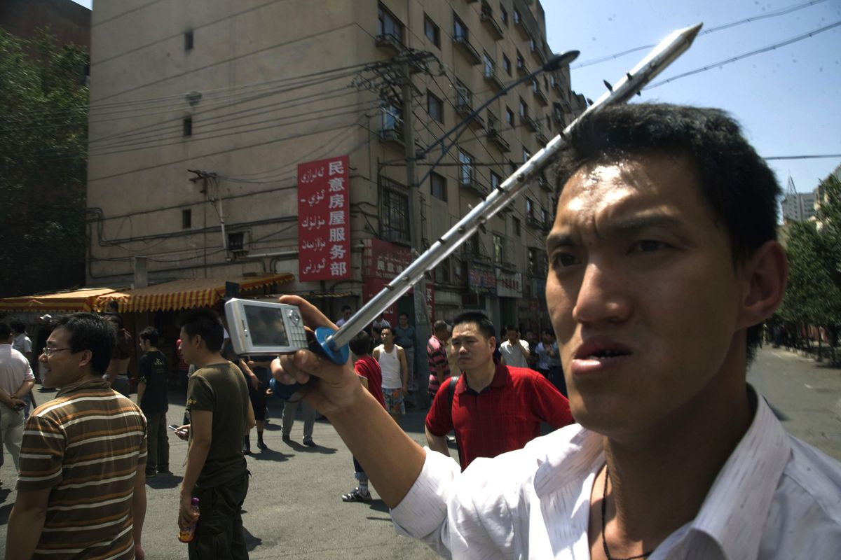 A Han Chinese man with a steel bar uses his cell phone to take photos in a mob of Han Chinese men attacking Uighur properties in Urumqi. (The Spokesman-Review)