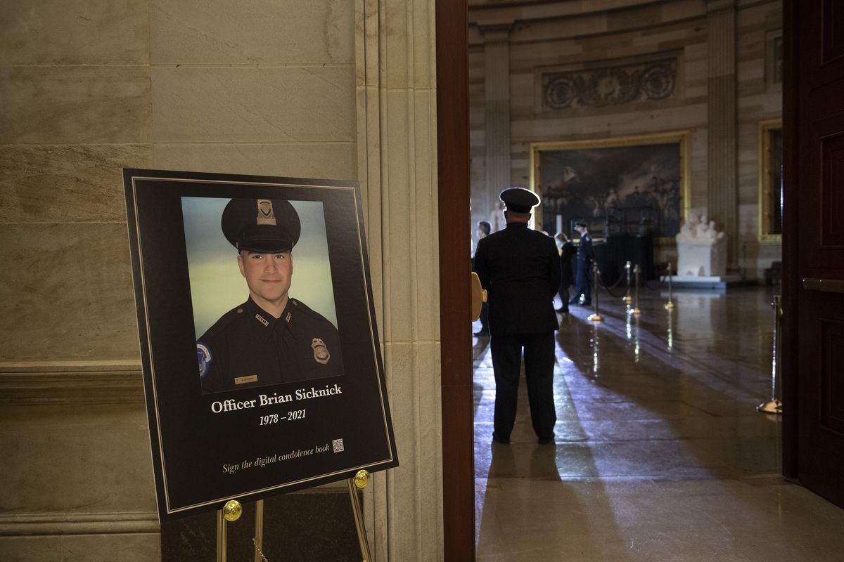 FILE – In this Feb. 2, 2021, file photo a placard is displayed with an image of the late U.S. Capitol Police officer Brian Sicknick on it as people wait for an urn with his cremated remains to be carried into the U.S. Capitol to lie in honor in the Capitol Rotunda in Washington. Federal investigators probing the death Sicknick, a U.S. Capitol Police officer killed in the Jan. 6 riot, have zeroed in on a suspect seen on video appearing to spray a chemical substance on the officer before he later collapsed and died, two people familiar with the matter told The Associated Press.  (Brendan Smialowski)