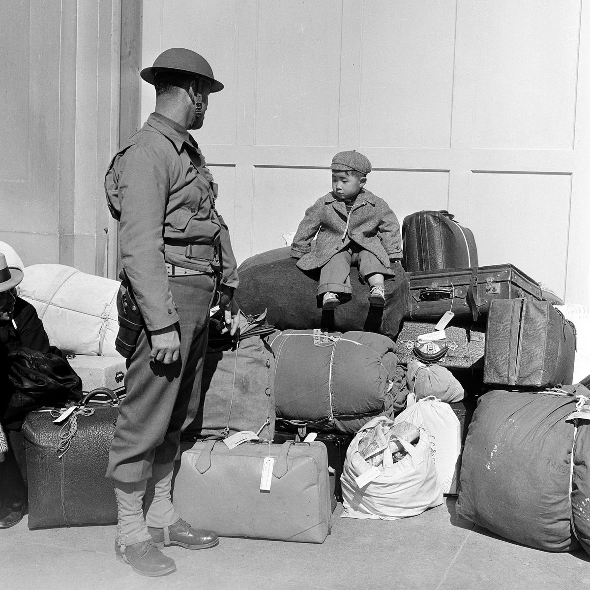 A boy sits on a pile of baggage as he waits for his parents, as a military policeman watches April 6, 1942, in San Francisco.  (STF)