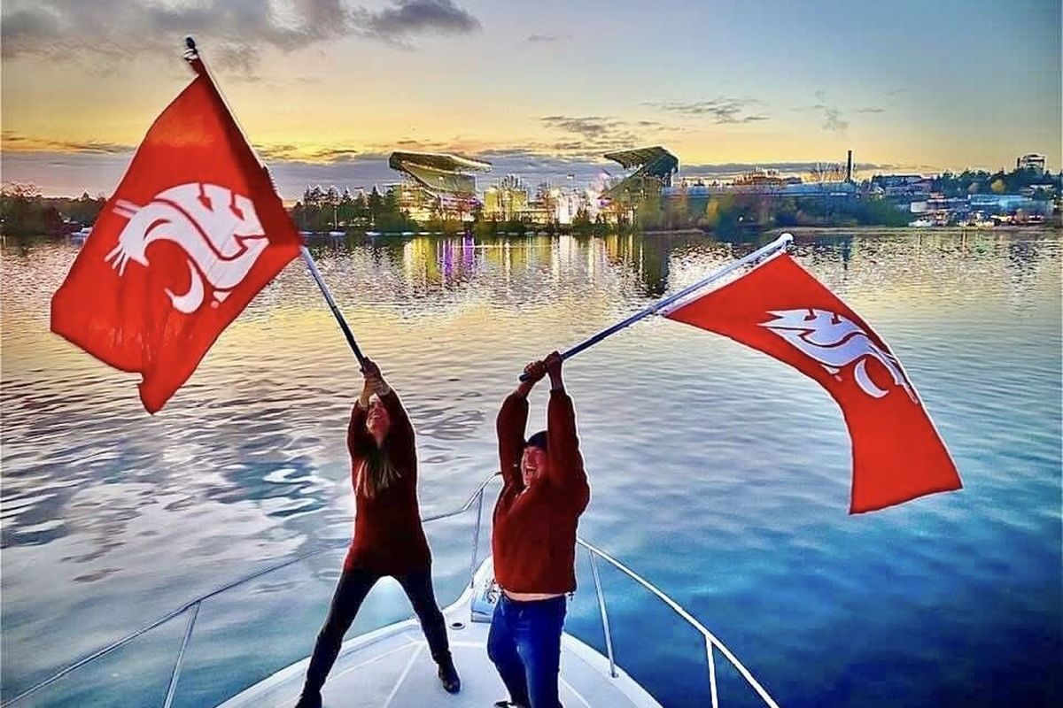 With Husky Stadium looming in the background, Nicole Rockfish and Bill O’Brien defiantly wave the WSU flag from a boat in Union Bay. (Courtesy of Paul Twibell)