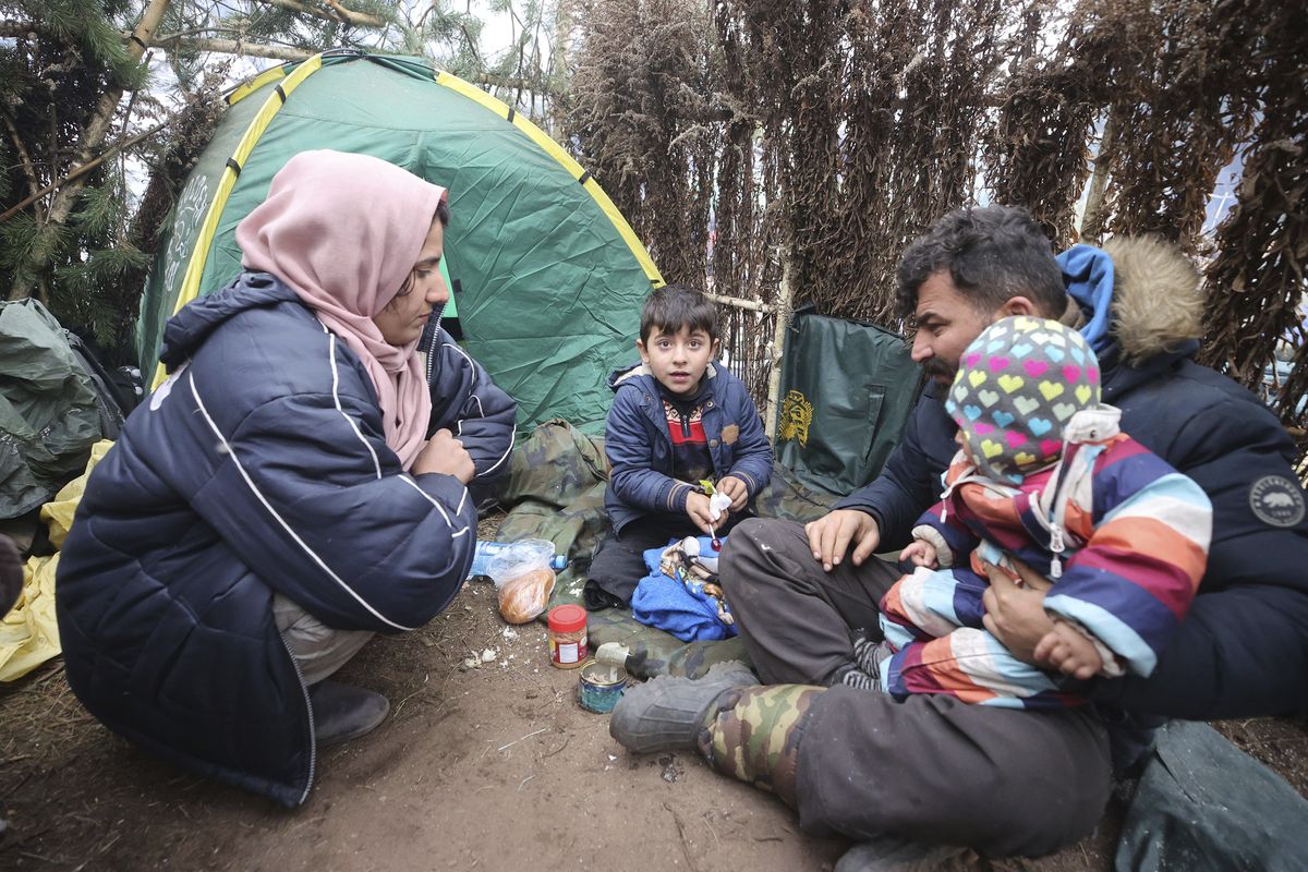 A family eat at a tent camp as migrants gather at the Belarus-Poland border near Grodno, Belarus, Saturday, Nov. 13, 2021. A large number of migrants are in a makeshift camp on the Belarusian side of the border in frigid conditions. Belarusian state news agency Belta reported that Lukashenko on Saturday ordered the military to set up tents at the border where food and other humanitarian aid can be gathered and distributed to the migrants.  (Leonid Shcheglov)