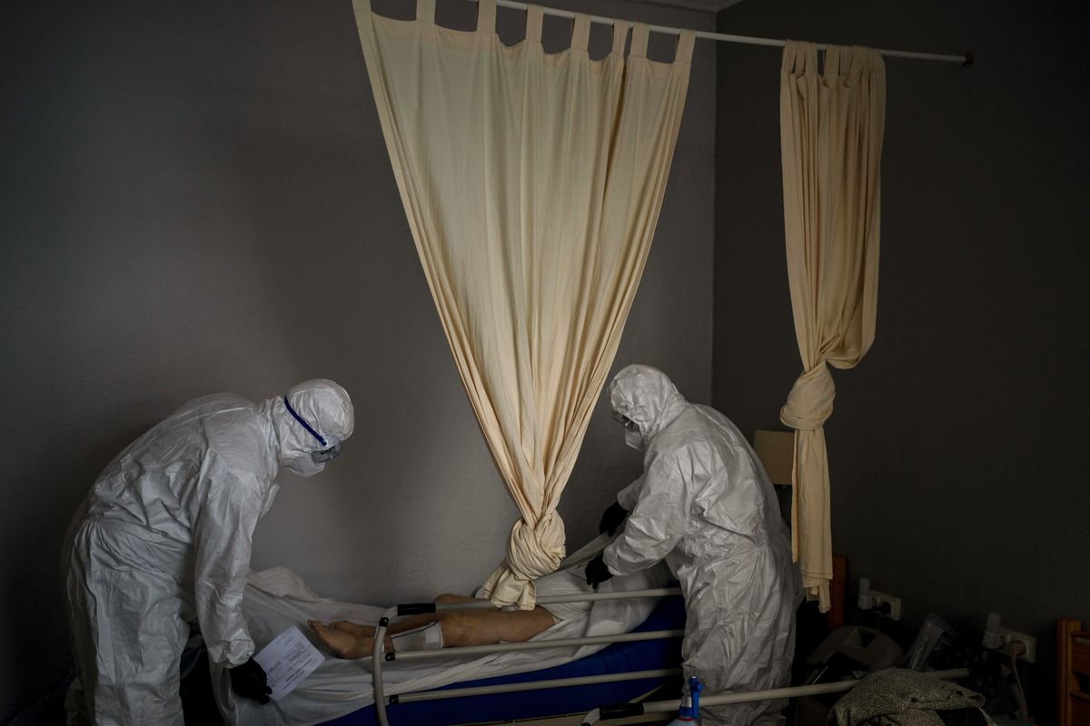 Wearing protective suits to prevent infection, mortuary workers prepare the body of an elderly person who died of COVID-19 before removing it from a nursing home Nov. 13 in Barcelona, Spain.  (Emilio Morenatti)