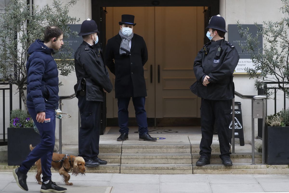 A man walks by with a dog as police officers stand outside King Edward VII