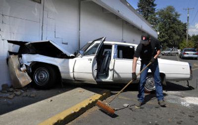 
Darrell Kendall of Inland Towing sweeps up broken glass and other debris after a Cadillac crashed into The Classy Rack thrift store at Sprague and Perrine on Friday morning. 
 (Dan Pelle / The Spokesman-Review)