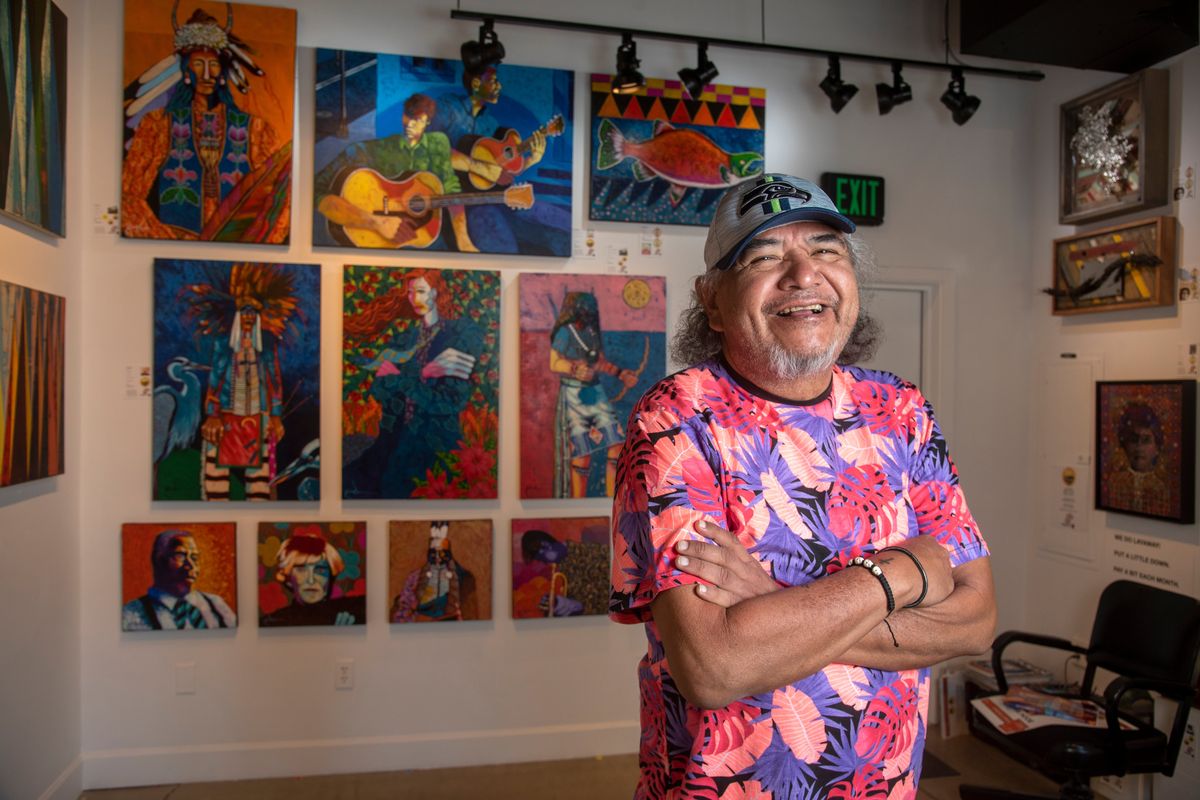 Artist Ric Gendron, longtime artist and member of the Confederated Tribes of the Colville Reservation, stands in front of some of his work on April 30 at the Marmot Art Space gallery in Kendall Yards, where he will release a new book in the coming weeks. His colorful work, featuring stylized portraits of artists, musicians and Native people, is seen around Spokane, including at the Ruby Hotel downtown.  (Jesse Tinsley/THE SPOKESMAN-REVIEW)