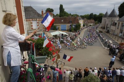 A woman waves the French flag on Bastille Day as the Tour de France pack passes through Montgivray.  (Associated Press / The Spokesman-Review)