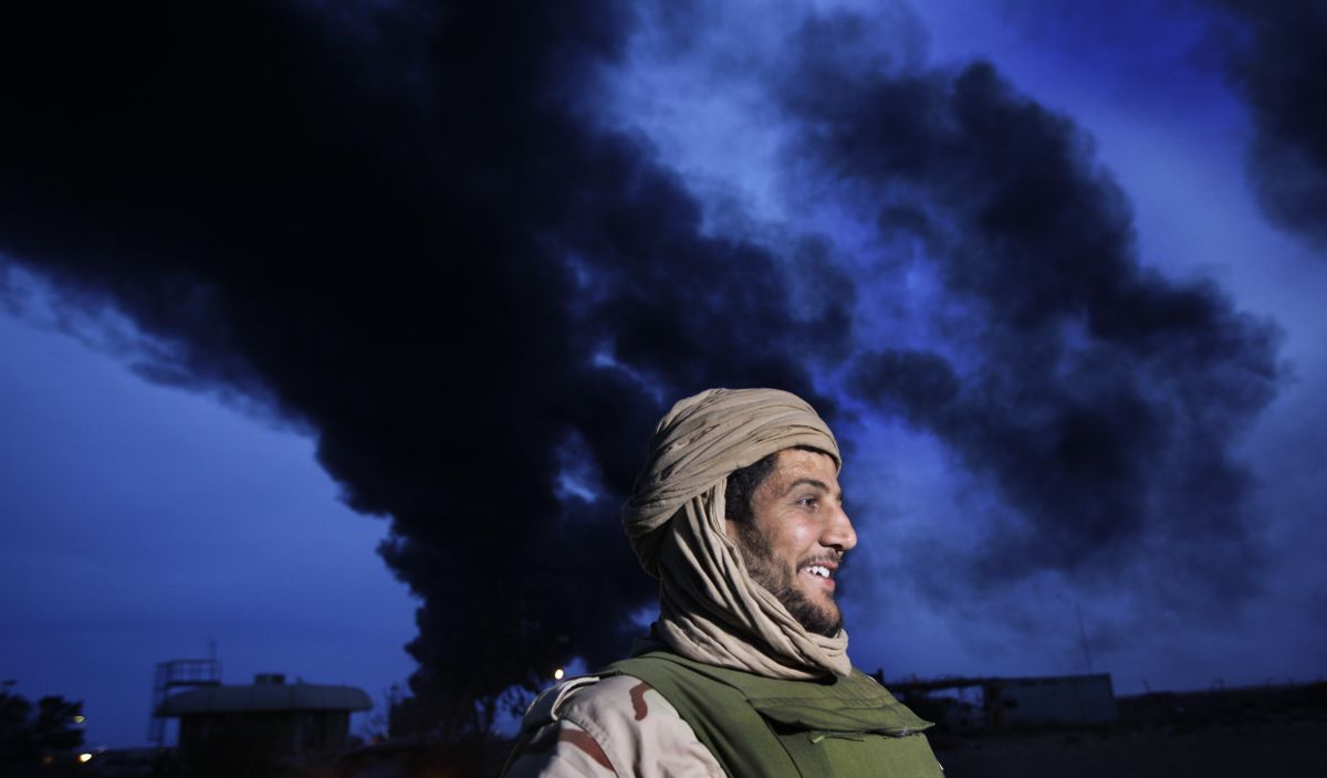 During a government-organized visit for foreign media, a pro-Gadhafi fighter is seen beneath a plume of smoke from the burning oil refinery in Ras Lanouf, Libya, on Saturday. (Associated Press)