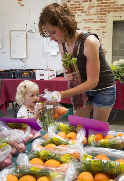 At the Spokane Public Market, Lauren Bauer and her daughter Addie, 2, buy apricots, asparagus and rhubarb from Mountain Valley View Farm on Friday. (Colin Mulvany)