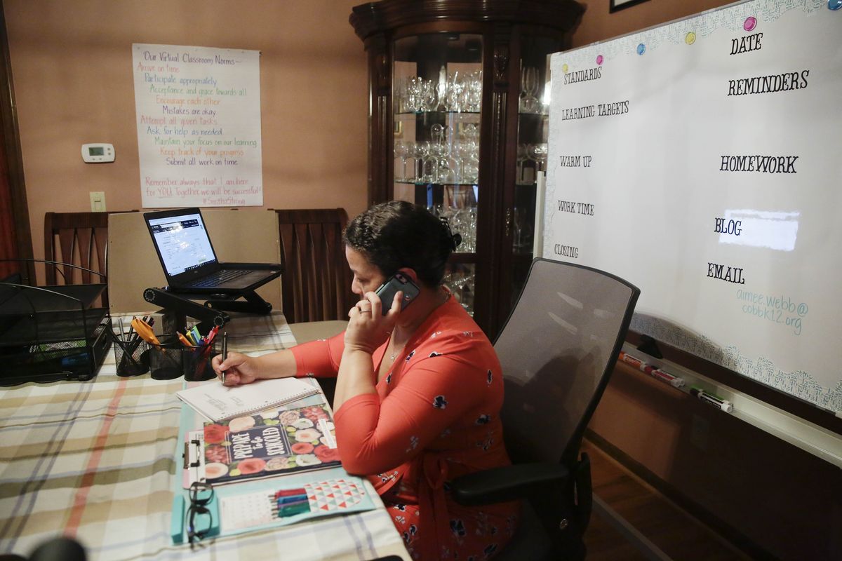 Aimee Rodriguez Webb works on her computer reading emails at her dinning room table that she set up as a virtual classroom for a Cobb County school, on Tuesday, July 28, 2020, in Marietta, Ga. After a rocky transition to distance learning last spring, Webb is determined to do better this fall. She bought a dry-erase board and a special camera to display worksheets, and she set up her dining room to broadcast school lessons.  (Brynn Anderson)