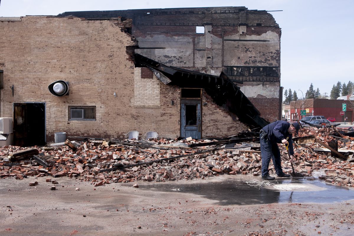 Palouse police Chief Jerry Neumann examines a large spot of paint amid the rubble of the Brick Wall Bar & Grill, which was destroyed by fire Tuesday morning in Palouse, Wash. A profanity was found scrawled on the pavement outside the building. (Tyler Tjomsland)