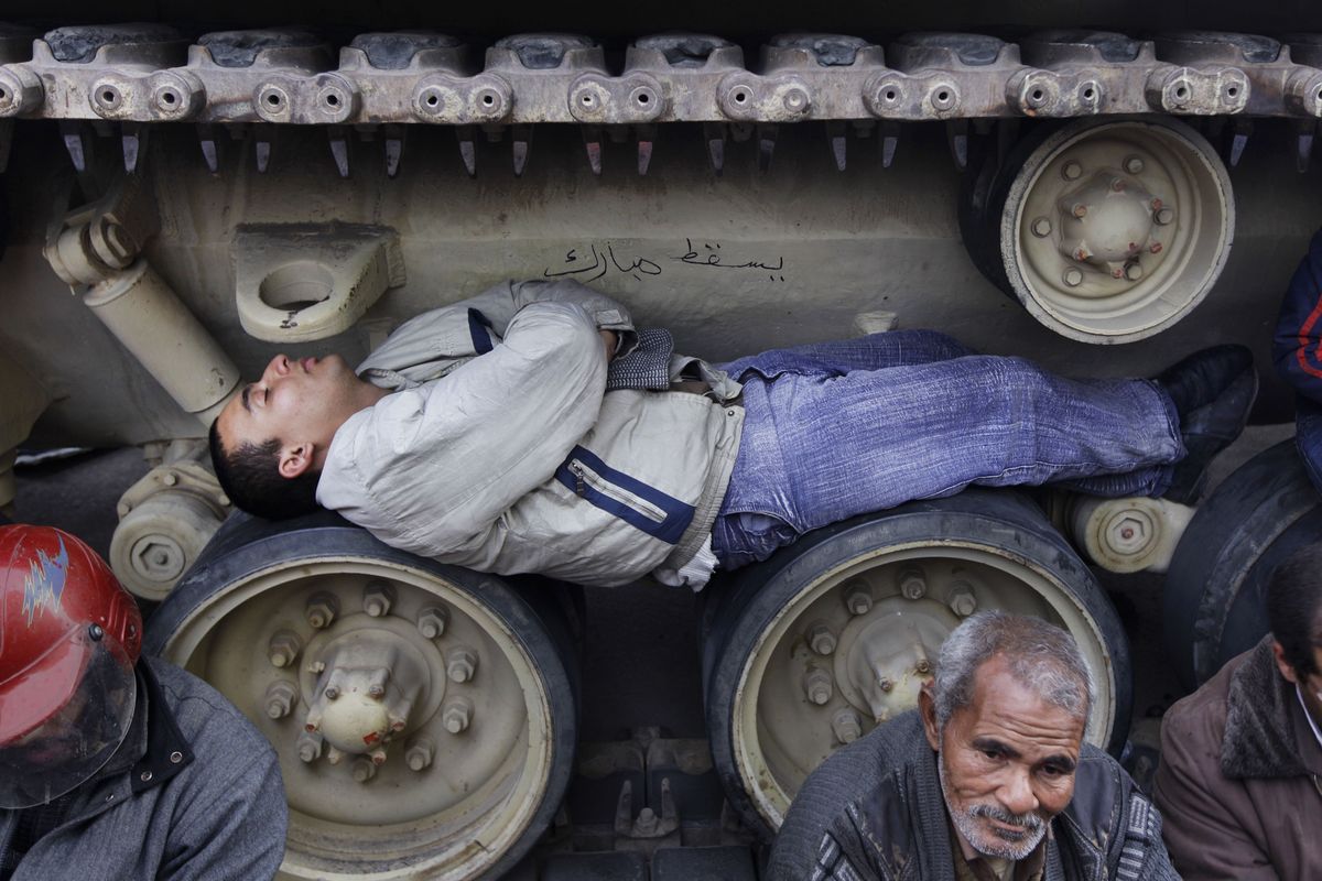 Anti-government protesters sit and lie inside the tracks of an Egyptian army tank, both to prevent them from moving and to shield themselves from the rain, at the protest site opposite the Egyptian Museum near Tahrir Square in downtown Cairo, Egypt, on Sunday, Feb. 6, 2011.  (Ben Curtis / Associated Press)