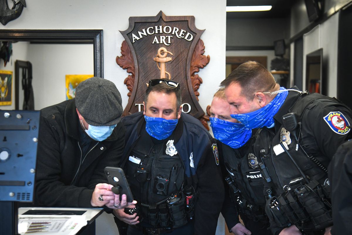 Jeremy Corns, left, owner of Anchored Art Tattoo, shows Spokane police officers video of a person suspected of setting the outside of his business on fire in the early hours Tuesday at the Paulsen Center in downtown Spokane.  (DAN PELLE/THE SPOKESMAN-REVIEW)