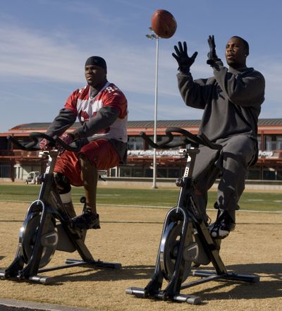 The Arizona Cardinals won’t know until game time if they can ride the talents of wide receiver Anquan Boldin, right, in today’s playoff game against the Panthers at Charlotte, N.C. Boldin, riding an exercise bike alongside tight end Ben Patrick during football practice in Arizona earlier this week, is trying to overcome a strained left hamstring.  (Associated Press / The Spokesman-Review)