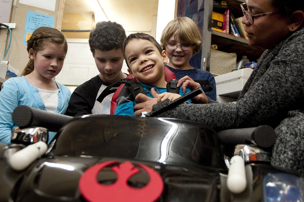 Five-year-old Barrett Limtiaco-Ruppel smiles as he is strapped into an remote controlled car by his mother Janai with help from Hannah Stowe,10, far left, Jonathan Stowe, 13, center, and Bear Coleman, 8, at Coeur d’Alene Makerspace/Gizmo in Coeur d’Alene on Wednesday, April 26, 2017. The kids helped design a car for Barrett, who suffers from cerebral palsy. (Kathy Plonka / The Spokesman-Review)