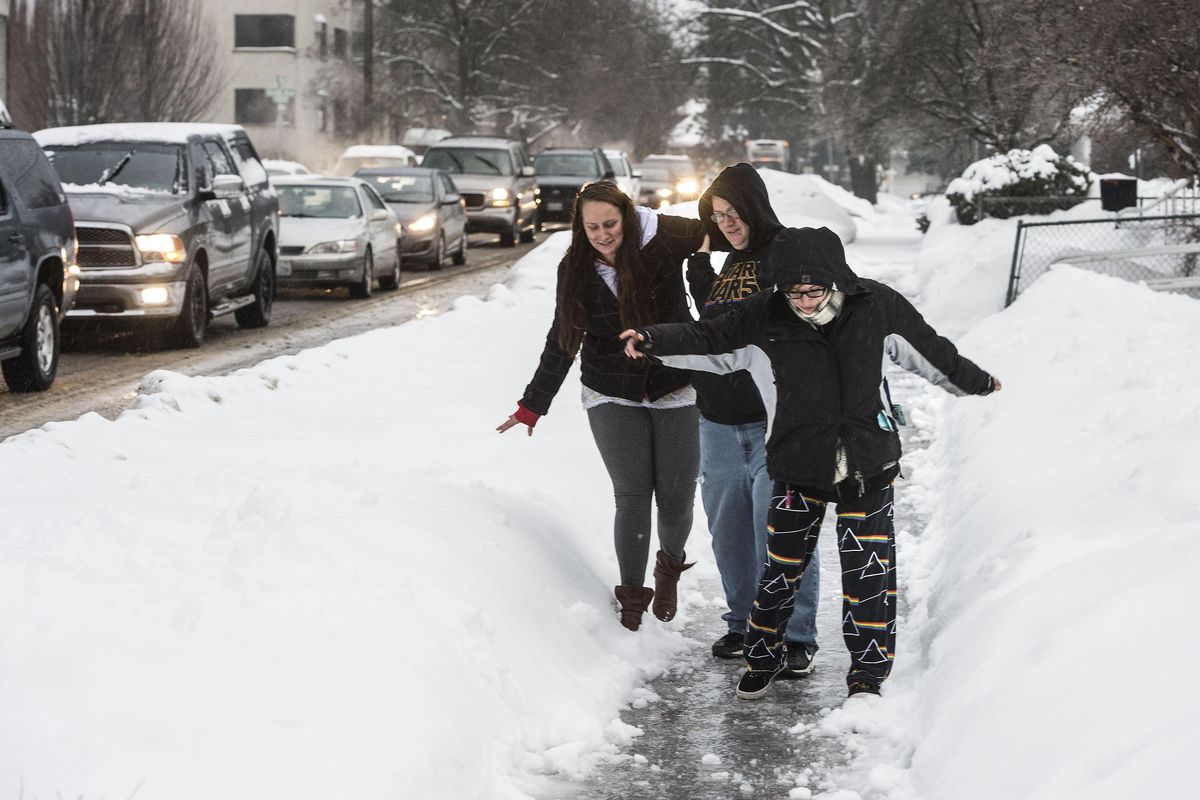 Brittany Silva, 25, Sheena Hutson, 30, and Stephanie Jones, 25, slide their way down the sidewalk on Walnut at Eighth Avenue as traffic backs up on the icy surfaces, Jan 18, 2017, in Spokane. (Dan Pelle / The Spokesman-Review)