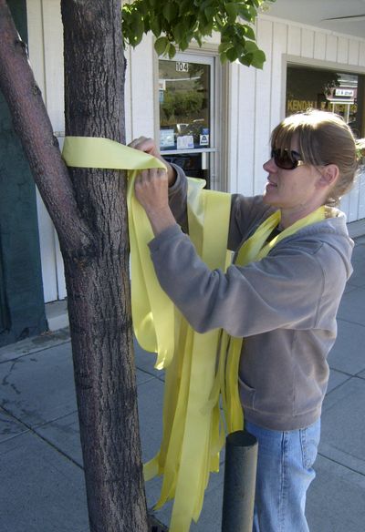 A woman who declined to be identified ties a yellow ribbon around a tree  on Monday in honor of Pfc. Bowe Bergdahl.  (Associated Press / The Spokesman-Review)