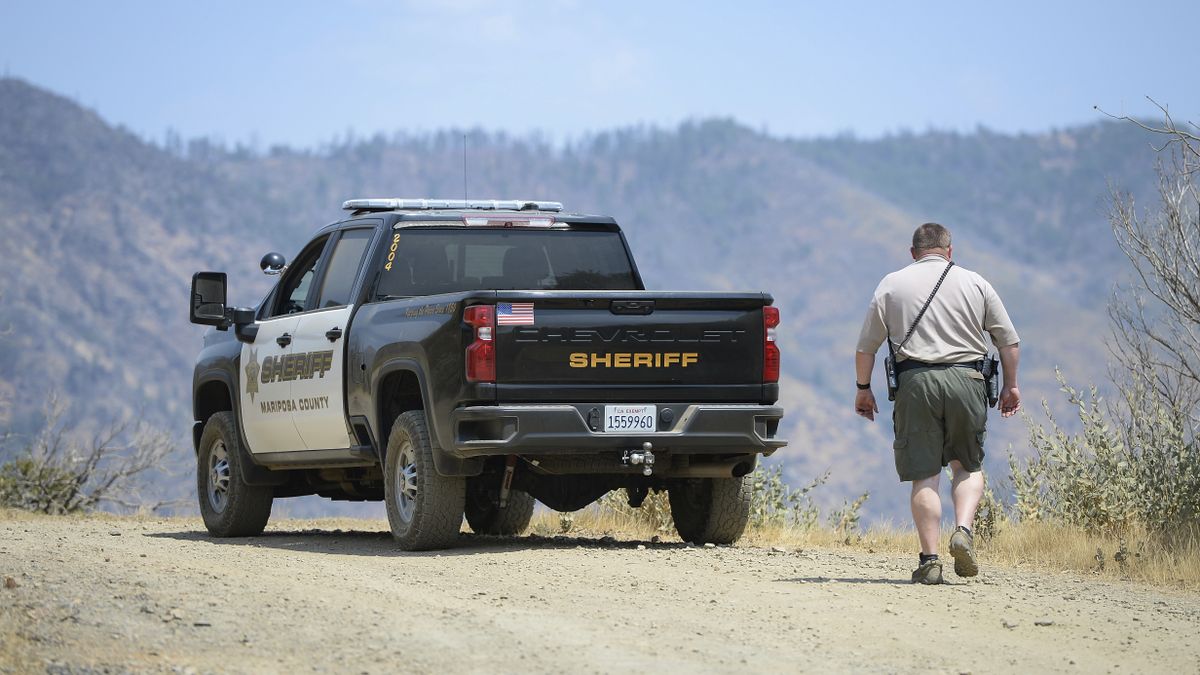 A Mariposa County deputy sheriff stands watch over a remote area northeast of the town of Mariposa, Calif., on Wednesday, Aug. 18, 2021, near the area where a family and their dog were reportedly found dead the day before. Investigators are considering whether toxic algae blooms or other hazards may have contributed to the deaths of the Northern California couple, their baby and the family dog on a remote hiking trail, authorities said.  (Craig Kohlruss)
