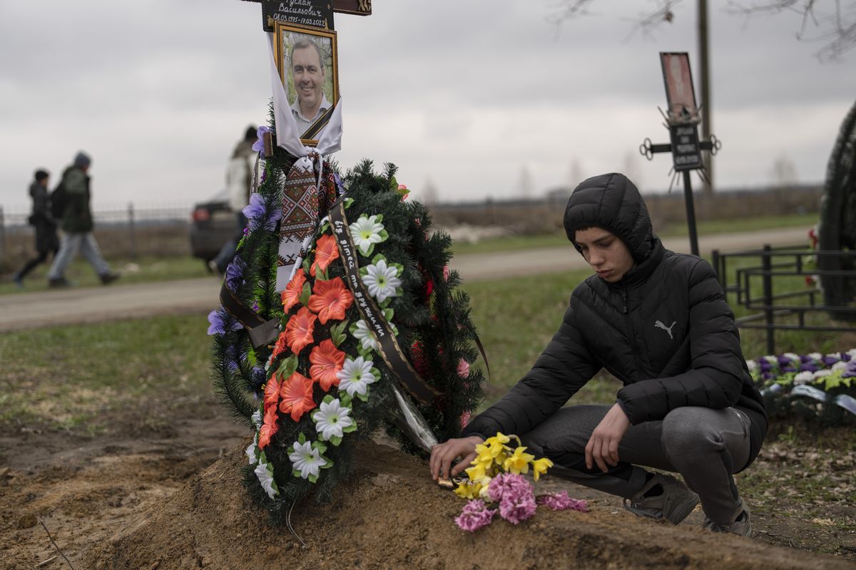 Yura Nechyporenko, 15, places a chocolate at the grave of his father Ruslan Nechyporenko at the cemetery in Bucha, on the outskirts of Kyiv, Ukraine, on Thursday, April 21, 2022. The teen survived an attempted killing by Russian soldiers while his father was killed, and now his family seeks justice.  (Petros Giannakouris)