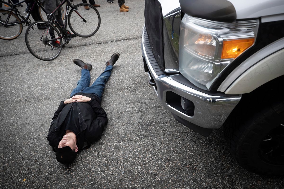 A counter protestor lies on the road in front of a truck leading a convoy of truckers opposed to COVID-19 health measures and vaccinations, in Vancouver, British Columbia, Saturday, Feb. 5, 2022. A group of more than 200 counter protesters on foot and on bikes held up the convoy for nearly an hour before police officers turned the trucks around and sent them on another route.  (Darryl Dyck)