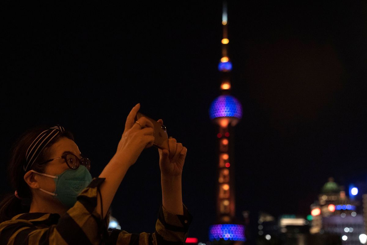 A woman takes photos near the Oriental Pearl Tower on the bund, Tuesday, May 31, 2022, in Shanghai. Shanghai authorities say they will take major steps Wednesday toward reopening China