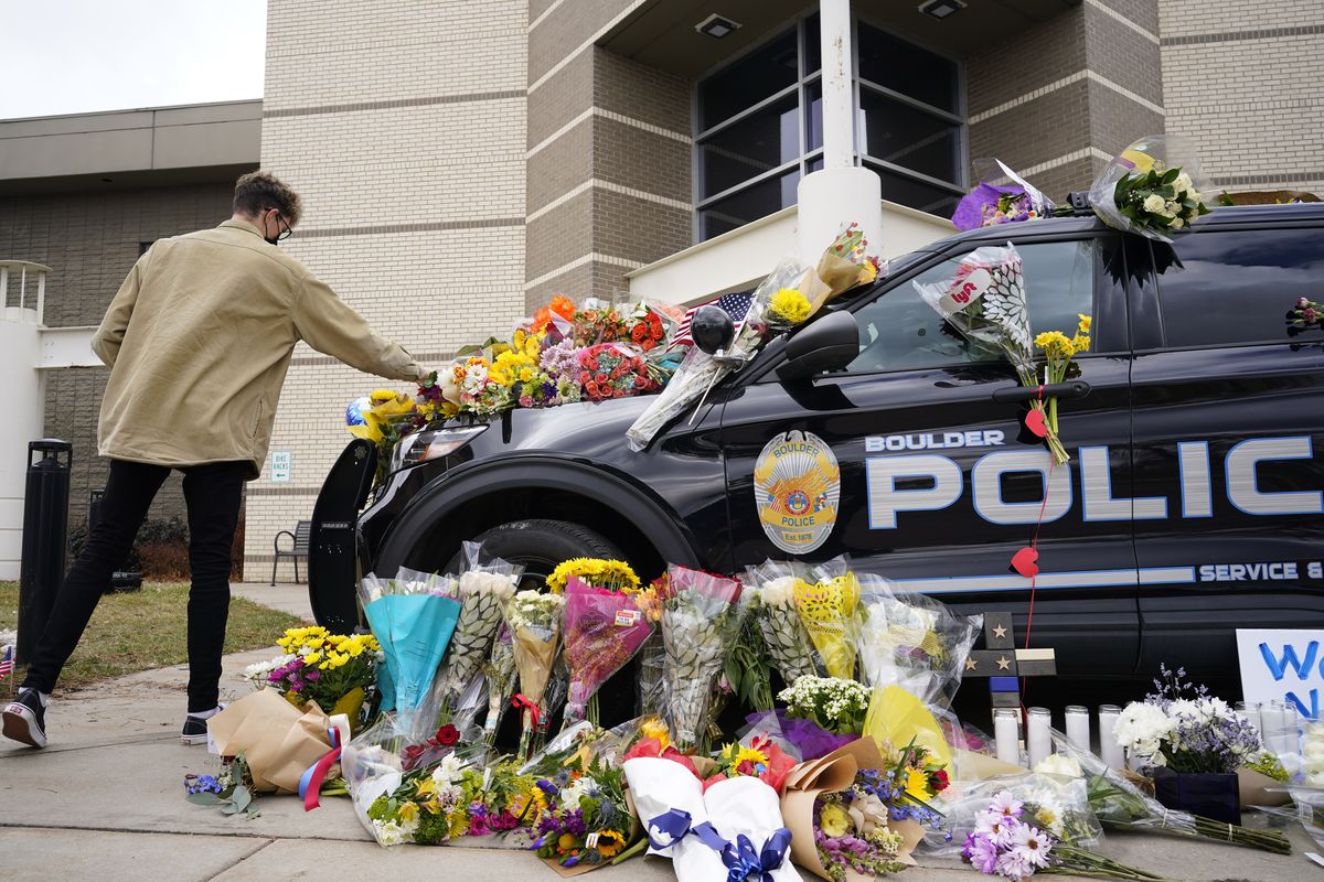 In this March 23, 2021, photo, a man leaves a bouquet on a police cruiser parked outside the Boulder Police Department after an officer was one of the victims of a mass shooting at a King Soopers grocery store in Boulder, Colo. The suspects in the most recent shooting sprees found it relatively easy to get their guns. The suspect in the shooting at a Boulder supermarket was convicted of assaulting a high school classmate but still got a gun.  (David Zalubowski)