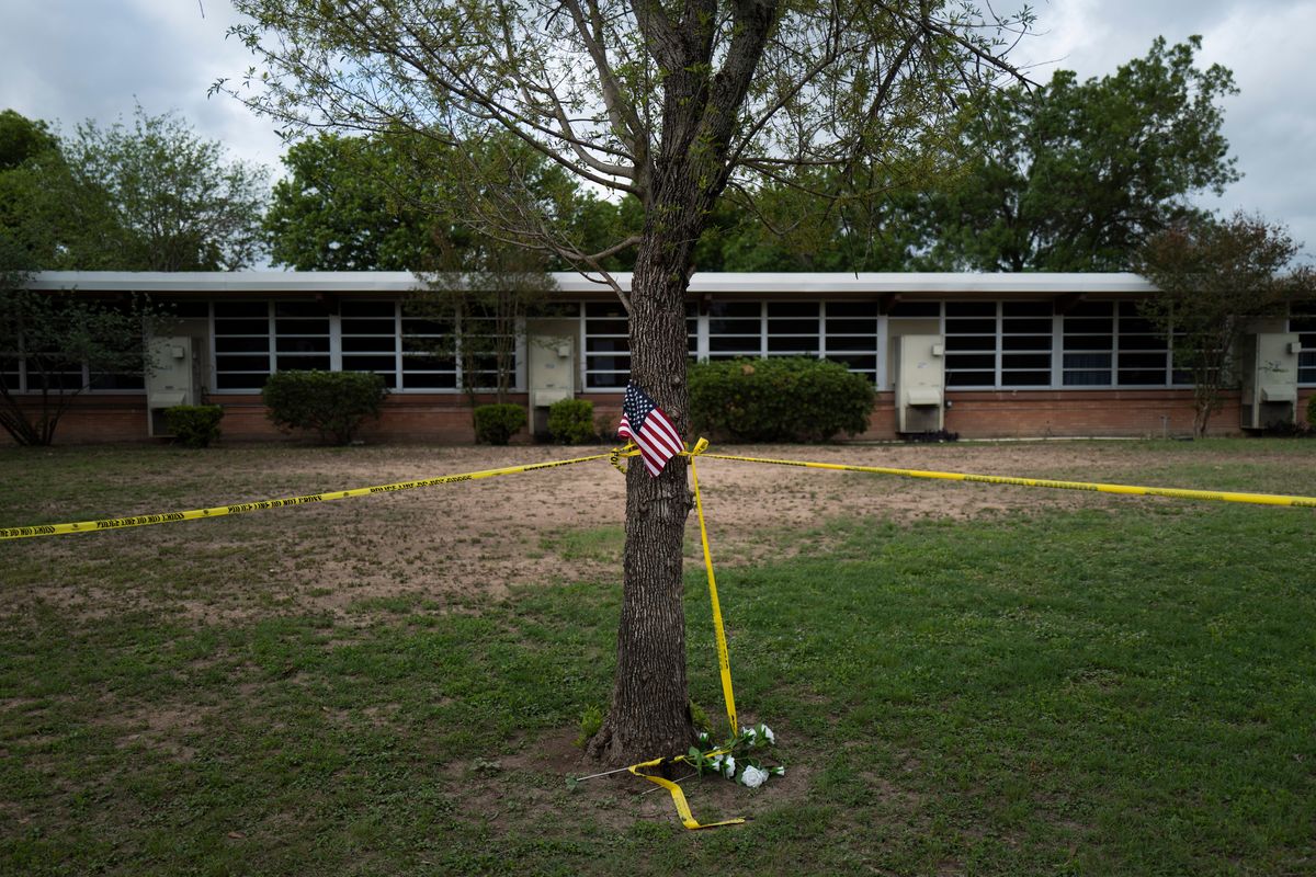A school building stands behind a tree with an American flag and crime scene tape at Robb Elementary School in Uvalde, Texas Monday, May 30, 2022. On May 24, 2022, an 18-year-old entered the school and fatally shot several children and teachers.  (Jae C. Hong)