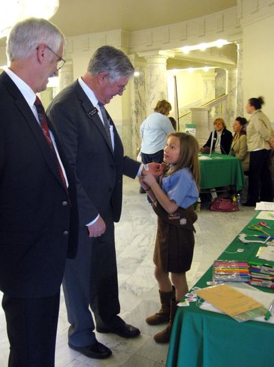 Reps. Ron Mendive, R-Coeur d’Alene, left, and Lance Clow, R-Twin Falls, talk to 9-year-old Brownie Ella Marcum-Hart in the Idaho state Capitol on Monday. Marcum-Hart is attaching a goal-setting bracelet to Clow’s wrist. (Betsy Russell)