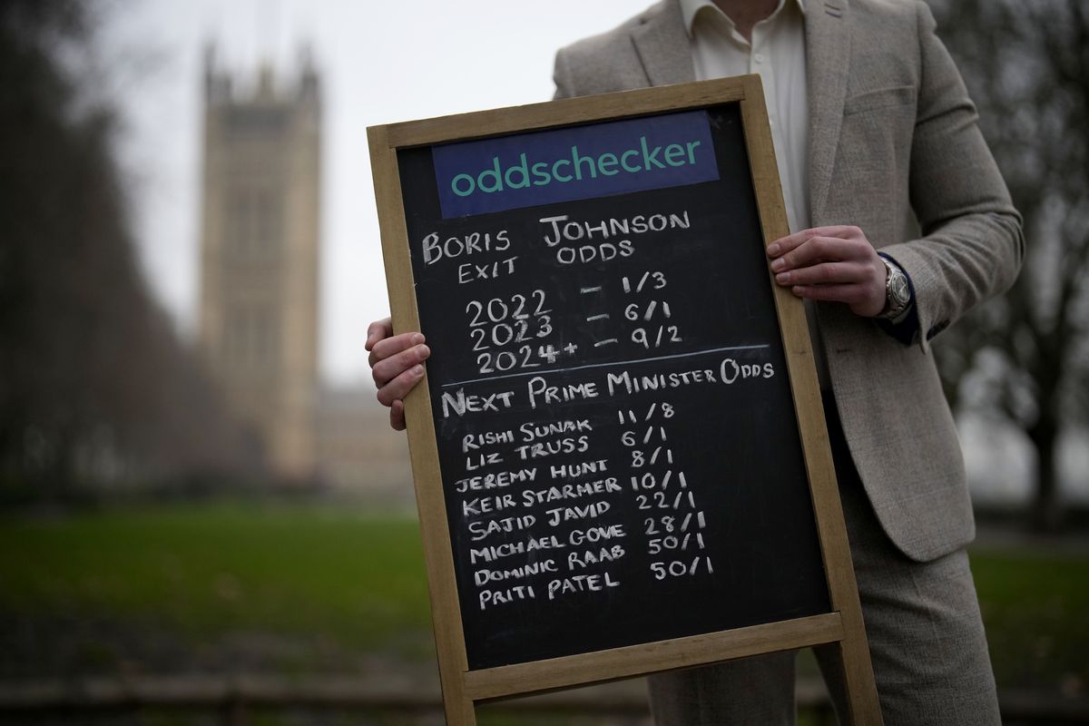 Callum Wilson, senior PR manager at the Oddschecker betting odds comparison company poses for photographs with a betting chalk board showing their odds for British Prime Minister Boris Johnson exiting his role as Prime Minister and odds for who the next Prime Minister might be, backdropped by the Houses of Parliament in London, Friday, Jan. 21, 2022. Some Conservative lawmakers in Britain are talking about ousting their leader, Prime Minister Boris Johnson, over allegations that he and his staff held lockdown-breaching parties during the coronavirus pandemic. The party has a complex process for changing leaders that starts by lawmakers writing letters to demand a no-confidence vote.  (Matt Dunham)