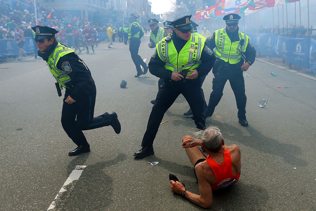In this April 15, 2013, photo, Bill Iffrig lies on the ground as police officers react to a second explosion at the finish line of the Boston Marathon. (John Tlumacki)