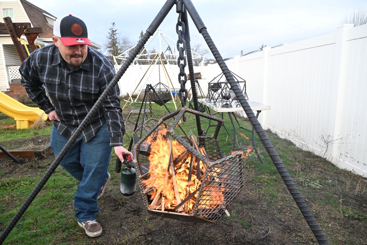 Metal artist and fabricator Scott Shumake lights up a fire on Thursday, in one of his hanging firepits, which he sells through his website ShumakeDesigns.com, but really made a splash by showing his handiwork in short videos on TikTok. BELOW: Scott shows a massive library of photos and videos that show off his hanging firepits.  (Jesse Tinsley/THE SPOKESMAN-REVIEW)