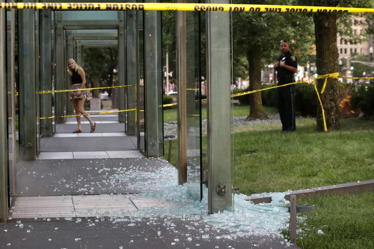 A passerby, left, and a law enforcement official, right, stand near broken glass at the New England Holocaust Memorial on Monday, Aug. 14, 2017, in Boston. Police say a person is in custody for allegedly vandalizing the memorial. It’s the second time the memorial has been damaged this summer. (Steven Senne / Associated Press)