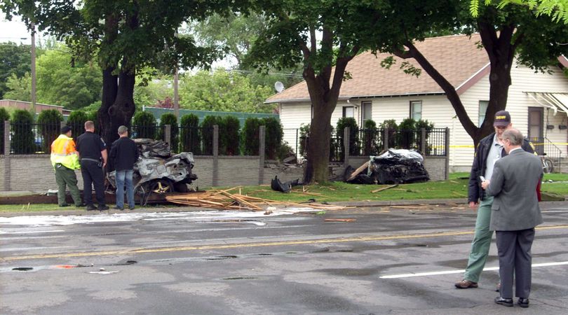 Pieces of a 2002 Acura, stolen in a carjacking this morning, were scattered along Indiana Avenue after the driver, who died, lost control and struck a tree. The impact split the car in two pieces seen at left by investigators and in the middle of the photo next to the right tree.  (Mike Prager / The Spokesman-Review)