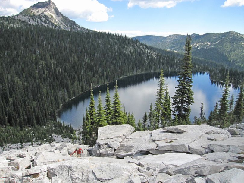 A hiker scrambles up the granite talus above Harrison Lake in the Idaho Selkirk Mountains with Harrison Peak in the background. This backcountry destination in the upper Pack River drainage was recommended for wilderness designation by the Forest Service in the 1980s, but the Idaho Panhandle National Forests plan does not include this area in wilderness recommendations.