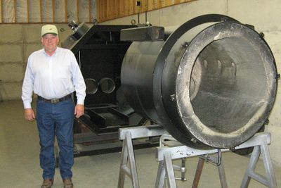 Dale Borgford stands beside a scaled-down version of an Octaflame Gasification System that uses waste wood to produce electricity and several byproducts. (Bert  Caldwell / The Spokesman-Review)