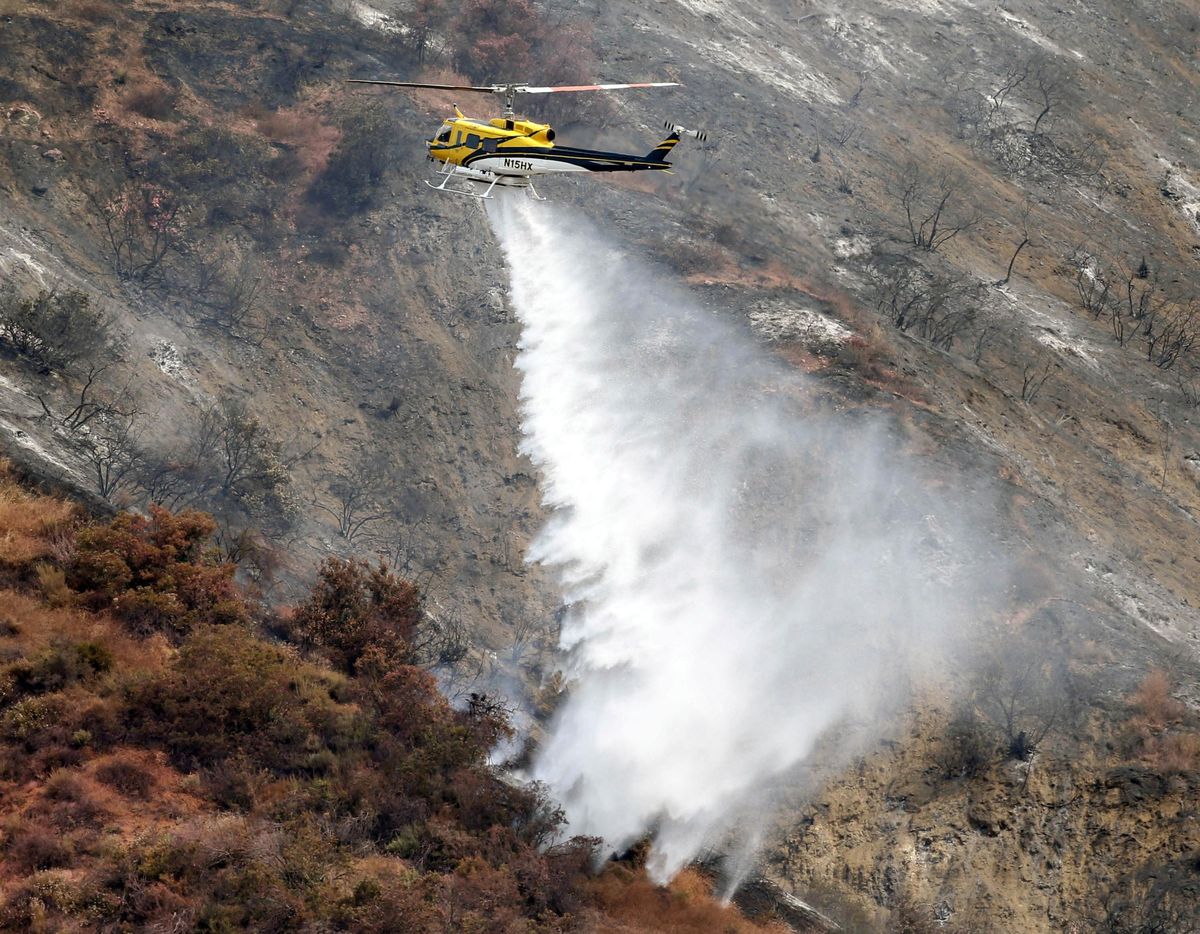 A firefighting helicopter makes a water drop on a hill near a wildfire in Duarte, Calif. Tuesday, June 21, 2016. (Nick Ut / Associated Press)
