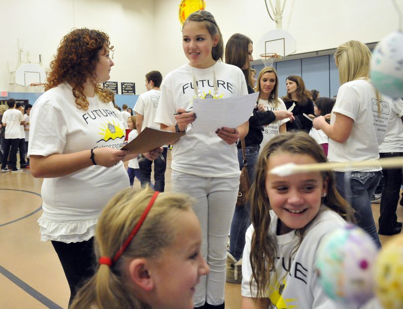 CV freshmen Jaimee Clark, standing at left, and Alexandra Burke, standing center, consult as they evaluate the entrepreneurial project of third-graders at Sunrise.