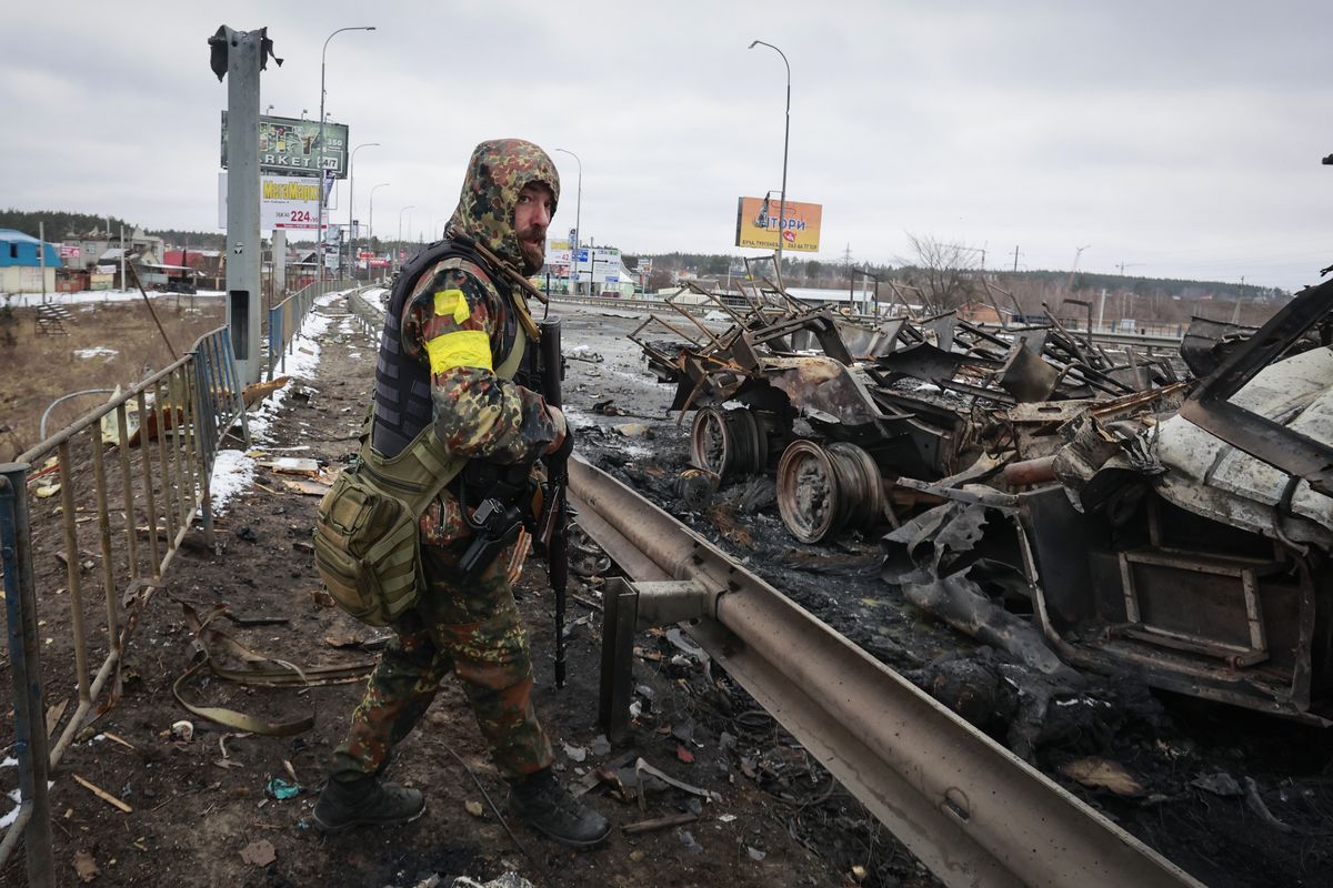 FILE - An armed man stands by the remains of a Russian military vehicle in Bucha, close to the capital Kyiv, Ukraine, March 1, 2022.  (Serhii Nuzhnenko)