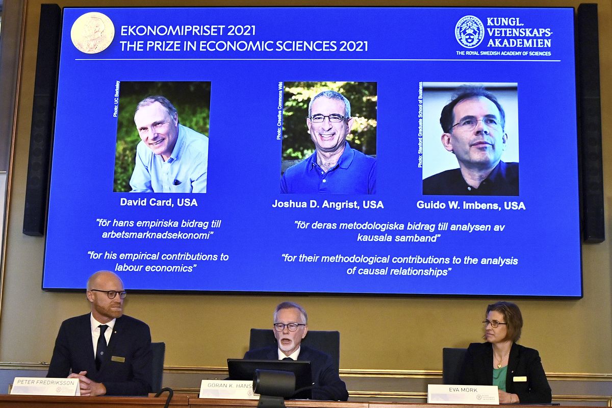 Goran Hansson of the Royal Swedish Academy of Sciences, center, announces the winners of the 2021 Nobel prize for economics – David Card, Joshua Angrist and Guido Imbens – who are shown on the screen above.  (Claudio Bresciani)