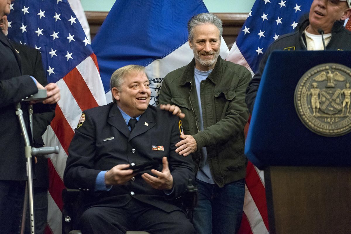 In this Jan. 9, 2016, file photo, comedian Jon Stewart, right, pats the shoulders of retired FDNY firefighter and Sept. 11 first responder Ray Pfeifer after Pfeifer was given the key to the city at New York’s City Hall. Stewart fought back tears Friday, June 2, 2017, during Pfeifer’s funeral, as he described his friendship with the retired New York City firefighter who worked in the rescue effort following the Sept. 11 terror attacks. (Craig Ruttle / Associated Press)