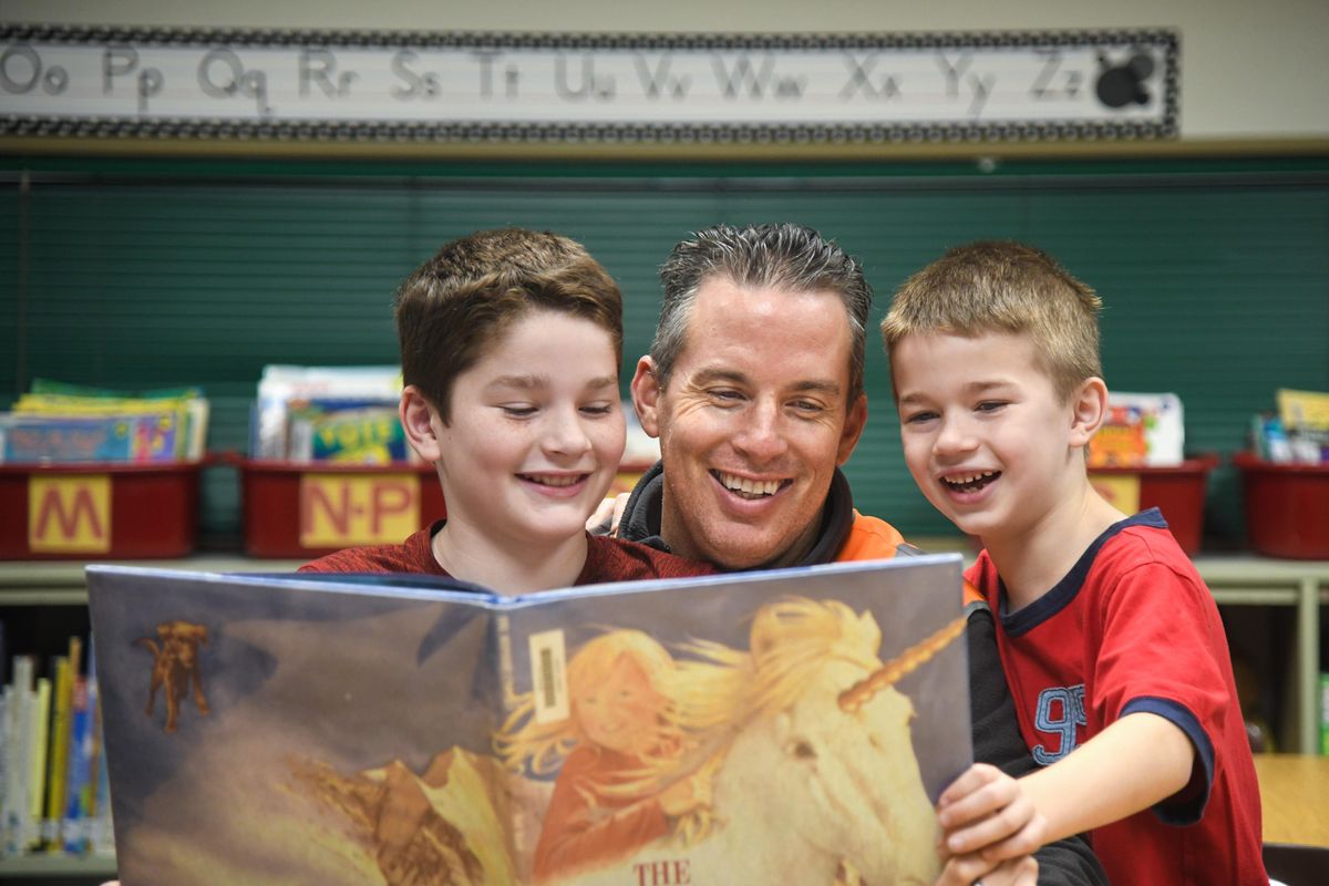 Joe Ader, a parent at Cooper Elementary School, has started the Cooper Champions program. It has gotten dads involved as volunteers at the school. Here he reads with his boys, Grant, 10, and Hayes, 7, in the Cooper Library, Friday, Oct. 26, 2018. (Dan Pelle / The Spokesman-Review)